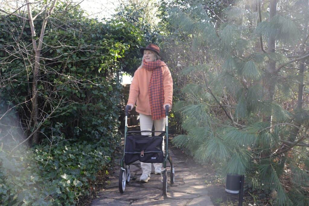 Senior walking upright with a walker on a garden path