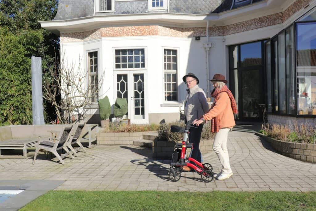 Senior and caregiver standing with a walker outside a modern home, checking the walker fits correctly