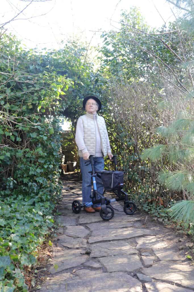 Older man walking with a walker on an outdoor stone path