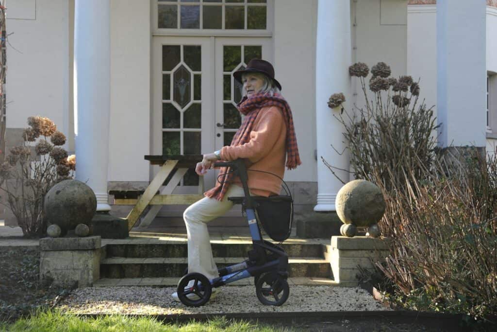 Older woman stepping carefully with her walker near the front steps of a house