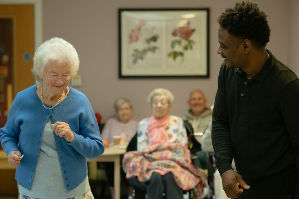 Older woman standing and moving with support from a caregiver, illustrating balance and fall risk checks