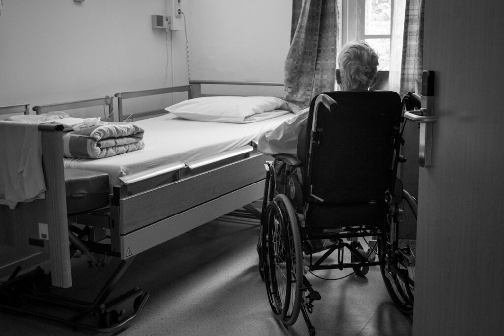 Person seated in a wheelchair in a home room, the kind of setting where a transfer board helps move to a bed or chair