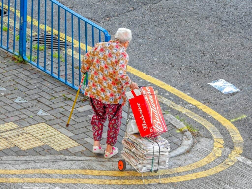Best Walker Baskets & Bags for Seniors: 7 Options Compared for Folding Walkers & Rollators 1 Older woman carrying her belongings on a wheeled cart while walking with a cane, illustrating walker baskets and bags