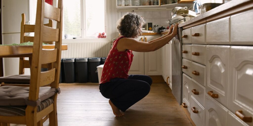 Woman bending to reach a low kitchen appliance - a reacher grabber helps seniors avoid bending