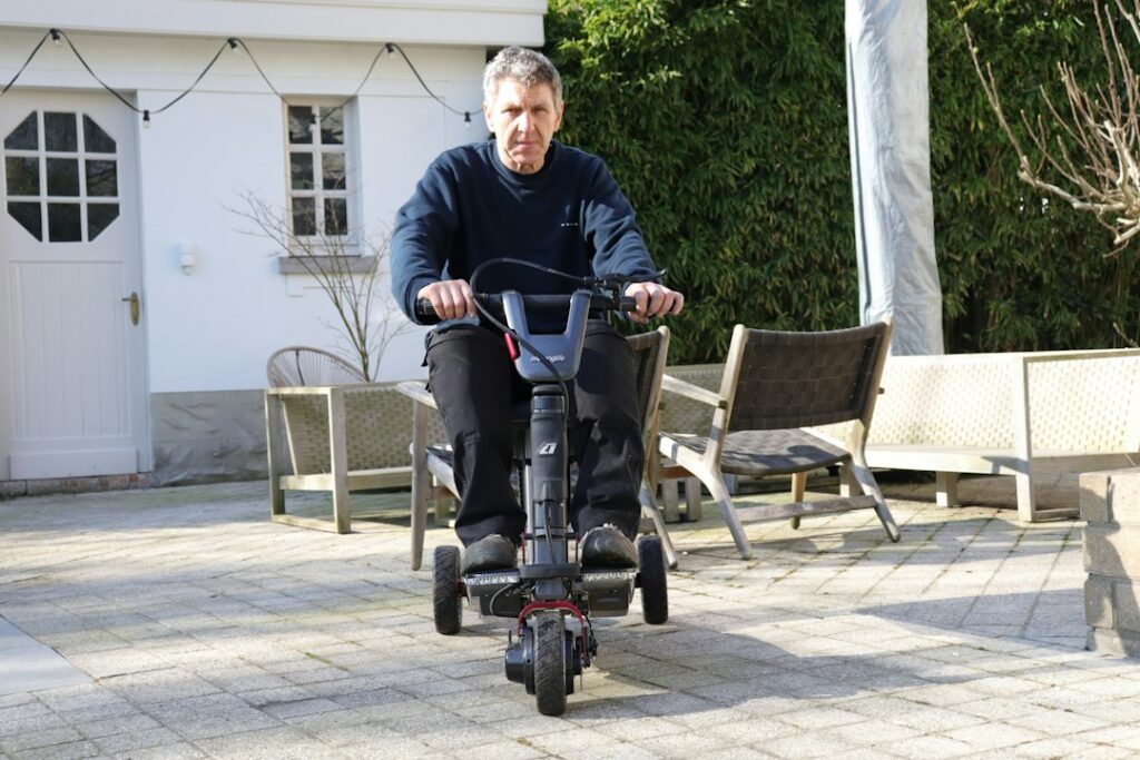 Man riding a three-wheeled mobility scooter outdoors, an alternative to a rollator for longer distances